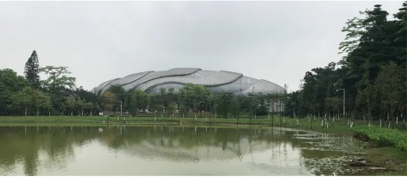 Distant view of the undulating shell roof across a reflecting pond and lawn with mature trees