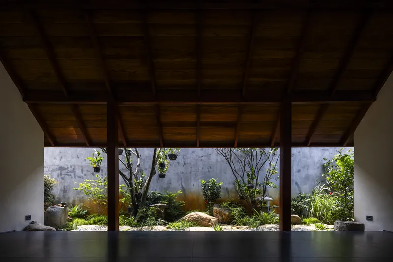 Covered pavilion with exposed timber post-and-beam structure framing a planted courtyard with concrete walls