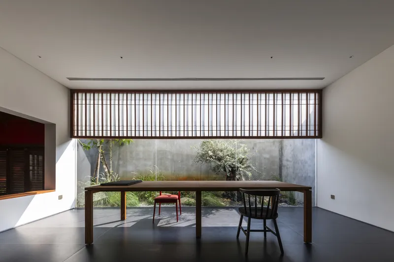 Dining area with timber table and slatted timber screen overlooking a concrete-walled courtyard garden
