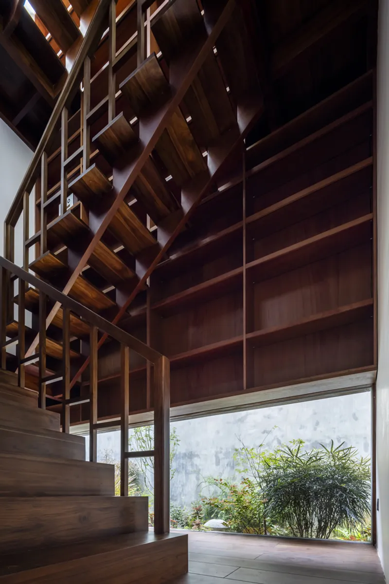 Timber staircase with diagonal lattice screen alongside a window overlooking a bamboo-planted courtyard