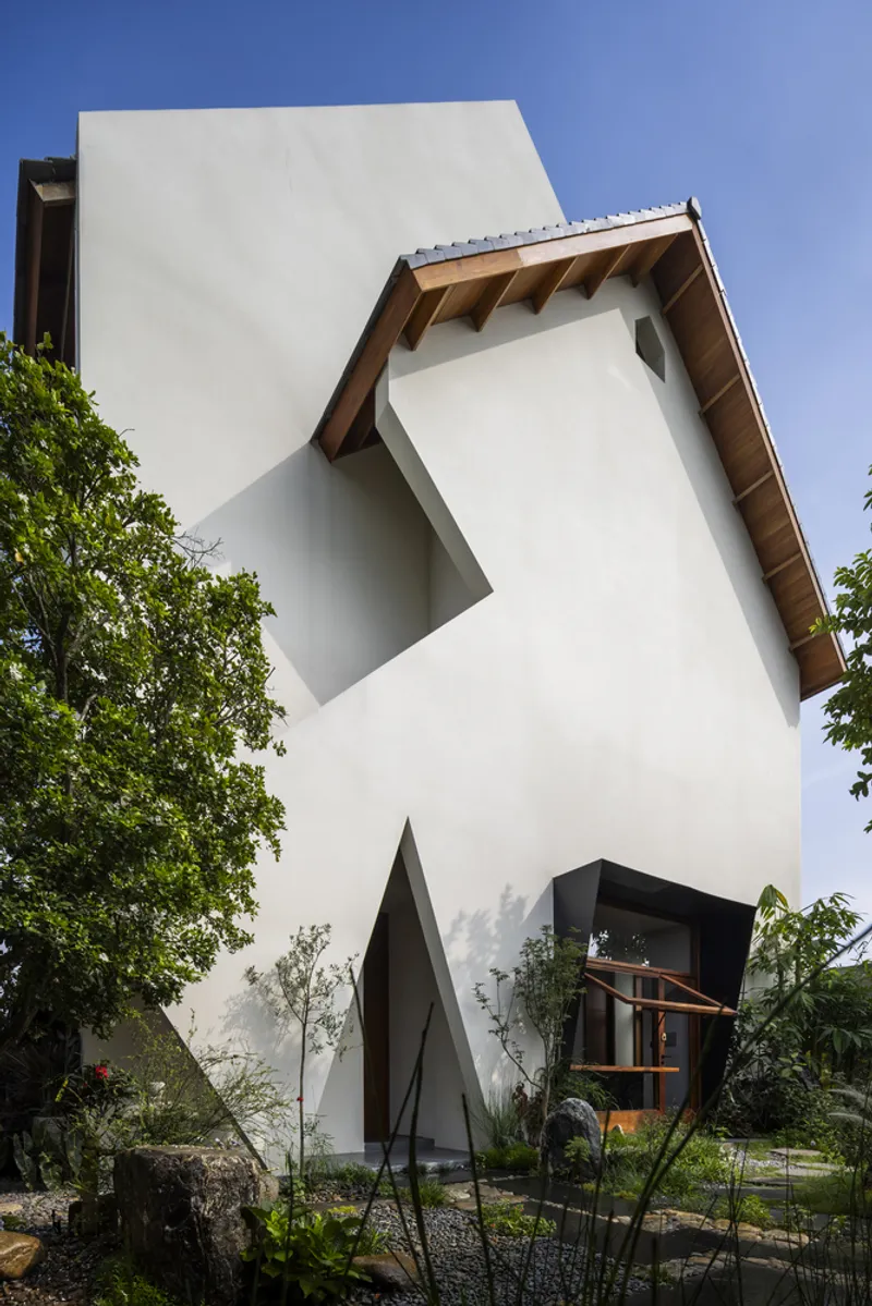 White geometric facade with angled volumes and exposed timber eaves beneath a clear blue sky