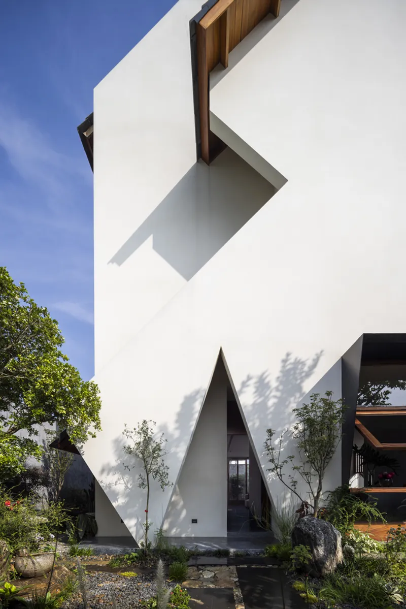White rendered facade with triangular entry recess and timber canopy above a gravel garden