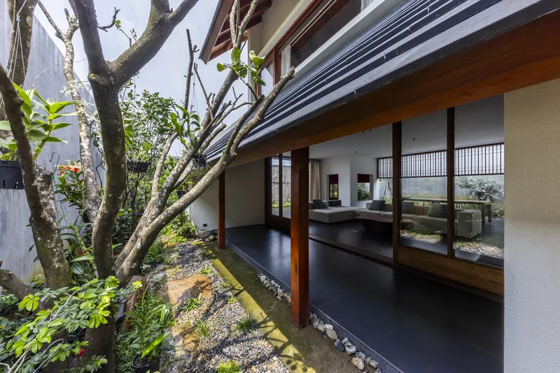 Open corridor with dark polished floor extending along a courtyard garden beneath corrugated metal roofing