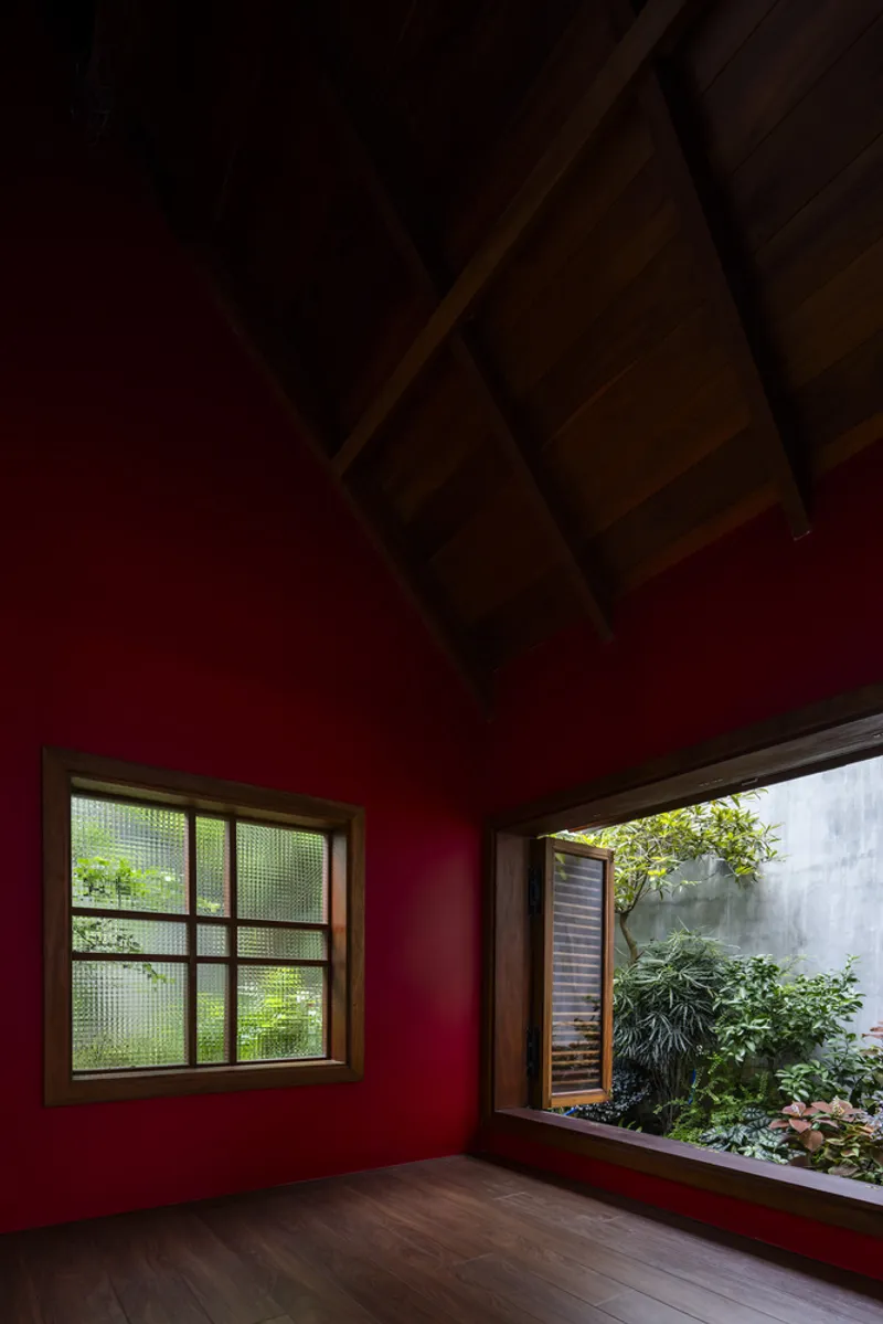 Red-painted interior room with exposed timber ceiling and textured glass window facing a planted courtyard
