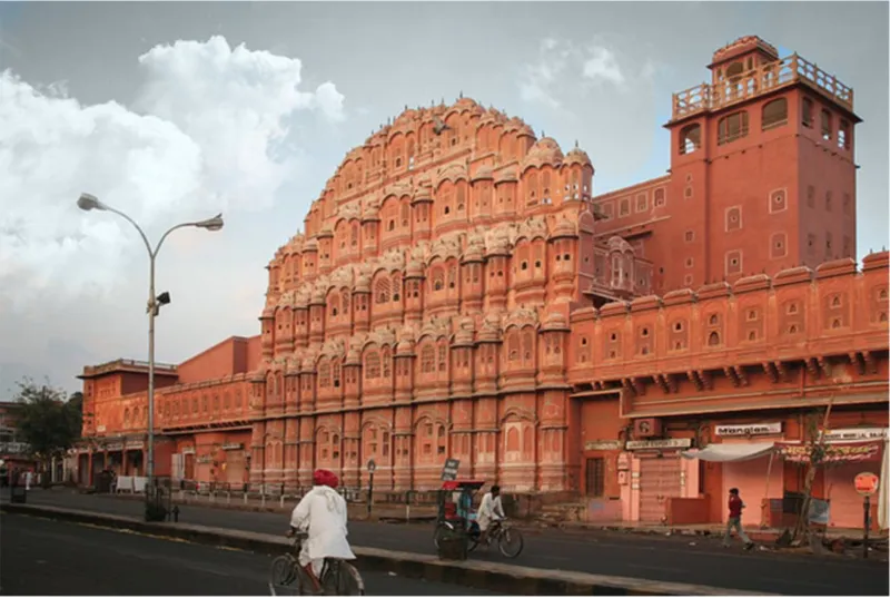 Street view of the honeycomb sandstone facade with cyclists and pedestrians passing under cloudy skies