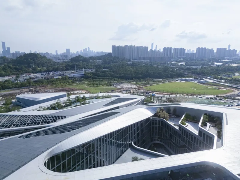 Rooftop view showing curved courtyard openings with planted terraces and patterned glass facades overlooking green fields