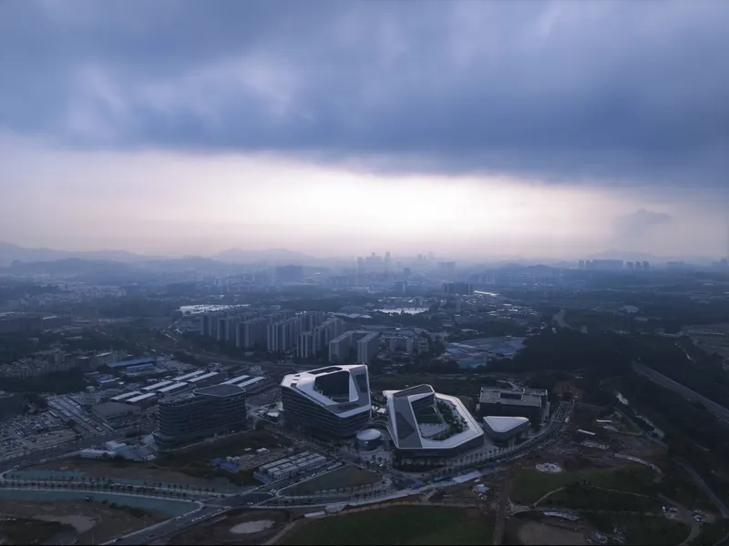 Drone view of white-roofed buildings with courtyard voids under stormy evening sky above distant cityscape