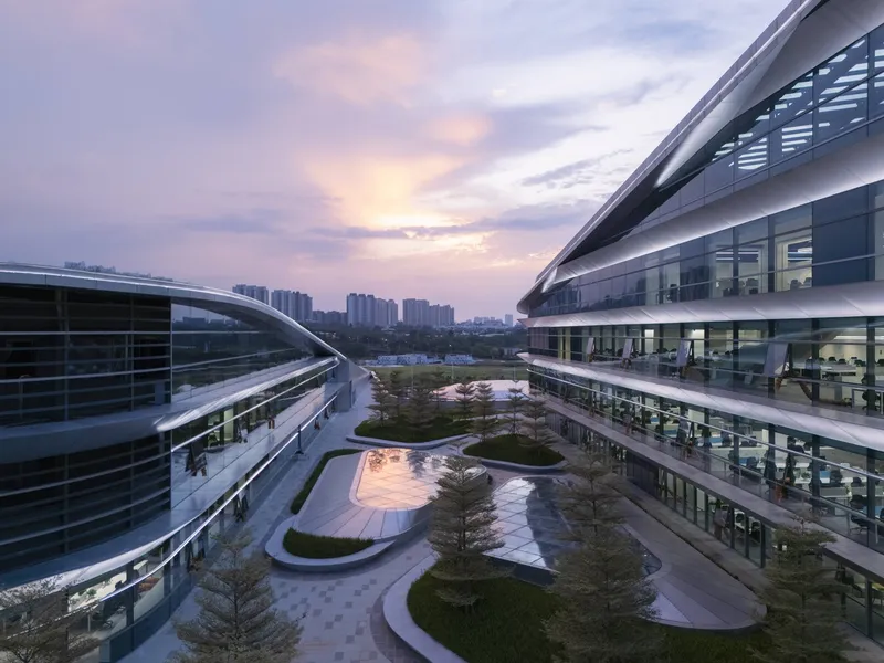 Courtyard garden with curved paving and planted beds between two glazed office wings at sunset