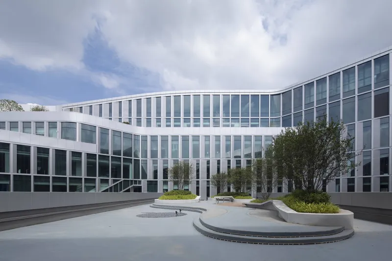 Ground-level courtyard with circular planters and benches surrounded by the white-framed glass facade