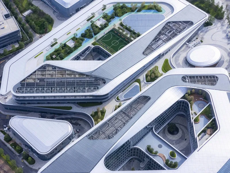 Aerial view of multiple buildings with white roofs and geometric courtyards containing rooftop gardens and sports fields