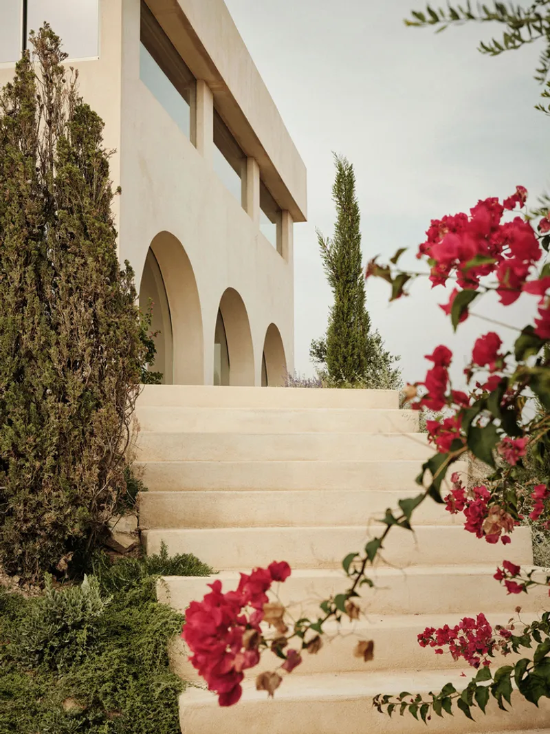 Exterior staircase ascending past arched openings with bougainvillea and cypress trees framing the view