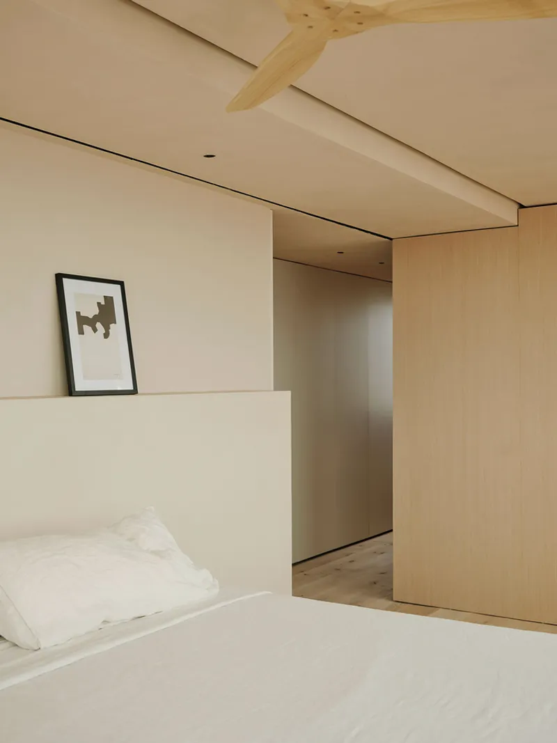 Bedroom with exposed timber beam crossing plaster ceiling above sliding wood partition and framed artwork