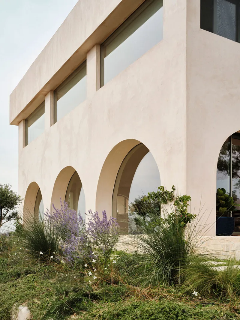 Exterior view of stuccoed facade with three arched openings and planted beds of lavender and grasses
