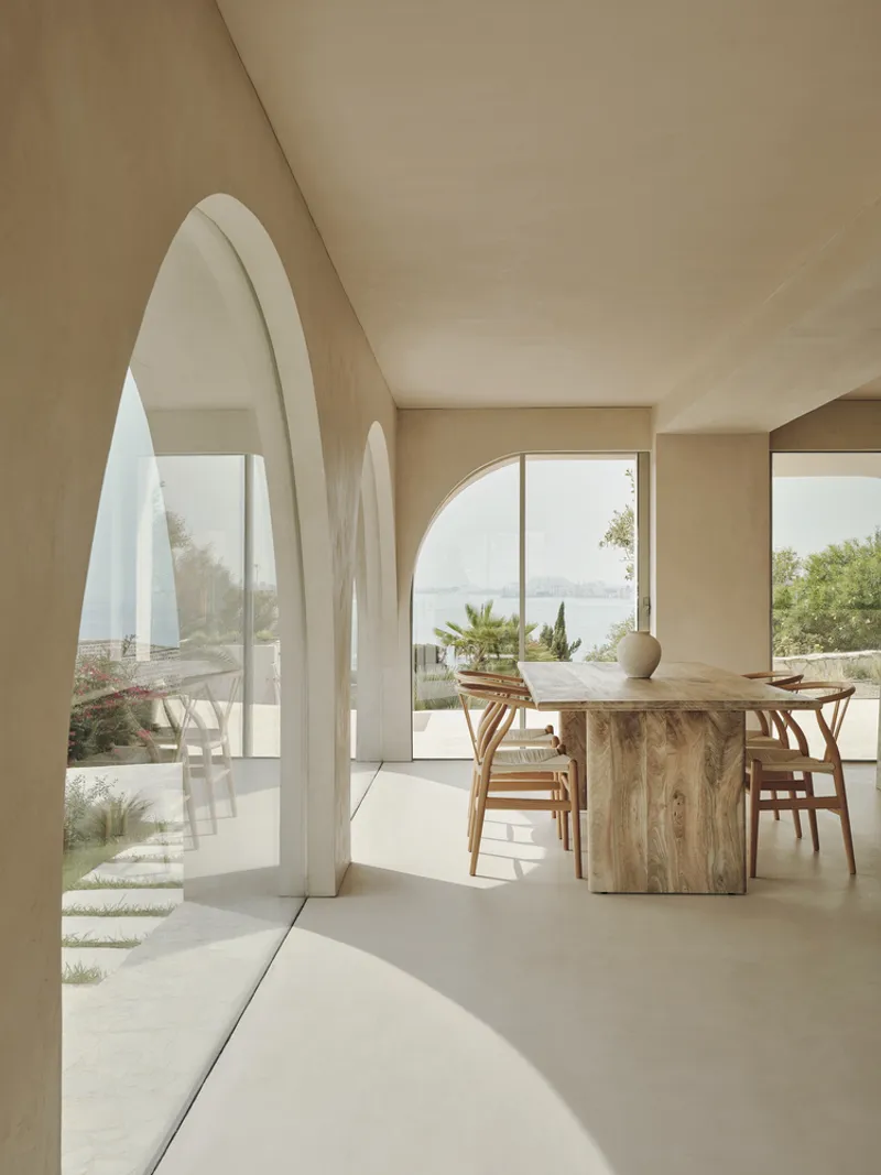 Interior dining space with arched openings framing coastal views and timber table under vaulted ceiling