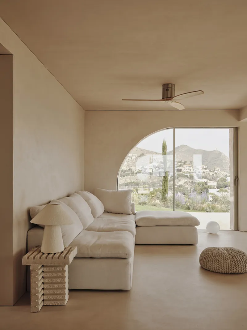 Living room with arched window overlooking hillside landscape and modular seating beneath ceiling fan