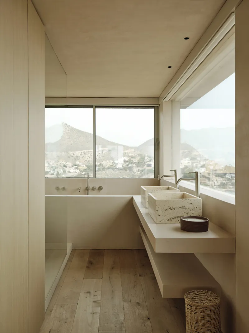 Bathroom with corner windows framing mountain views and travertine basin on floating vanity shelf