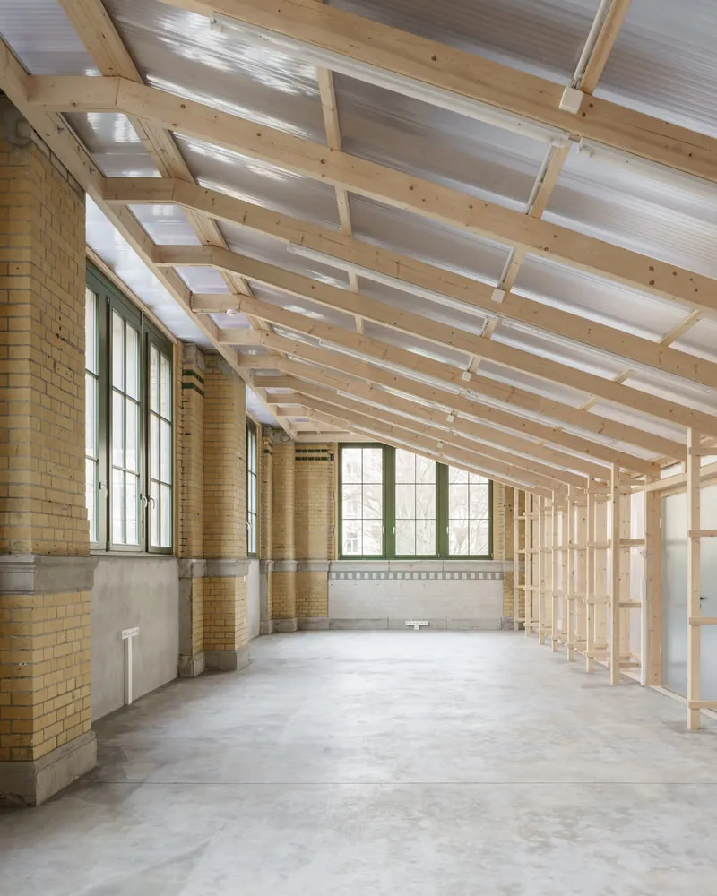 Corridor with timber frame ceiling, translucent polycarbonate panels and yellow brick perimeter wall with tall windows