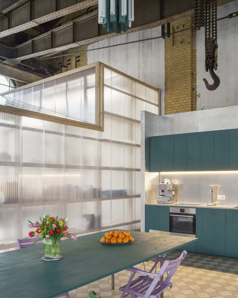Translucent corrugated panel partition separating dining area from teal kitchen with exposed industrial ceiling