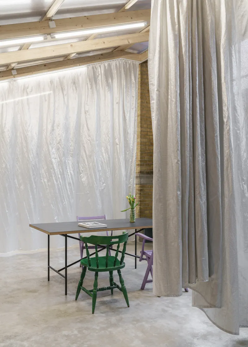 Workspace corner with table and chairs behind floor-to-ceiling fabric curtains and exposed timber roof beams