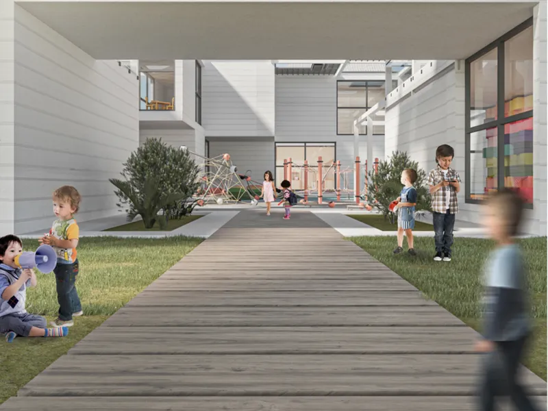 Central courtyard with timber boardwalk leading to play equipment, grass, and trees framed by white-clad building volumes