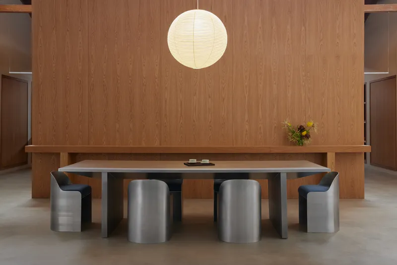 Meeting table with cylindrical upholstered stools beneath a spherical paper pendant and timber millwork backdrop