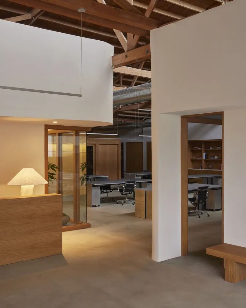Reception area with backlit timber desk and view through doorways to workspaces under exposed structural beams