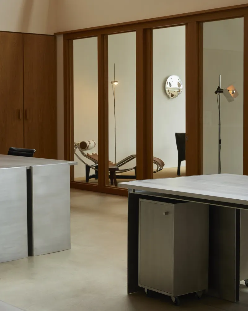 Office interior framed by timber glazing mullions with desk, pendant lights, and wall-mounted circular mirror