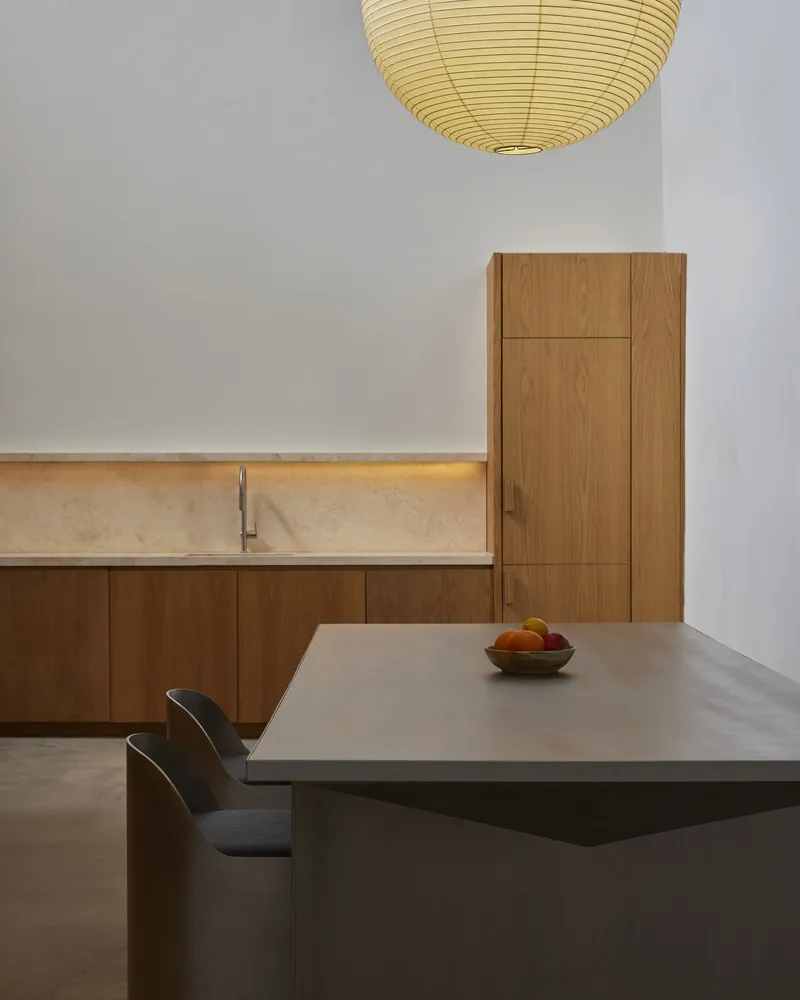 Kitchen island in grey composite with fruit bowl below paper lantern and oak millwork with stone counter