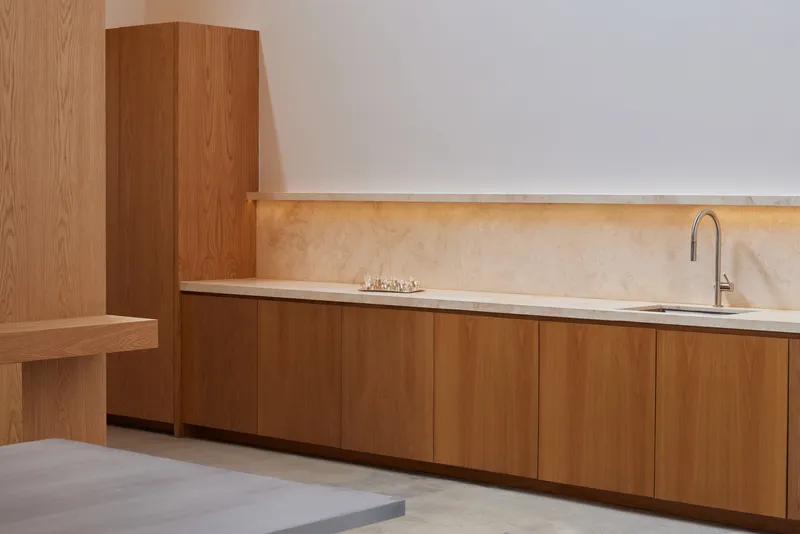 Kitchenette counter in oak cabinetry with pale stone backsplash and integrated sink under ambient strip lighting