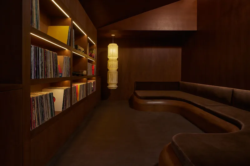 Dimly lit lounge with curved leather banquette, built-in shelving of records and a hanging paper lantern