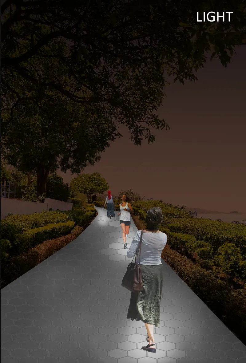 Illuminated hexagonal paving pathway cutting through planted hedges as people walk at dusk beneath a tree canopy