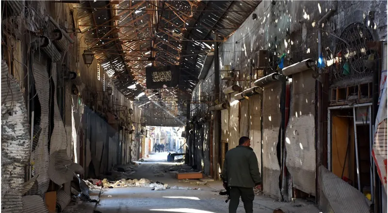 Covered market corridor with perforated metal roof and shuttered storefronts as a figure walks toward daylight