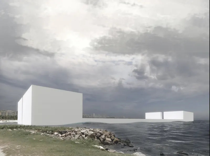 White rectangular volumes sitting in water beyond a rocky shore with grasses under overcast sky