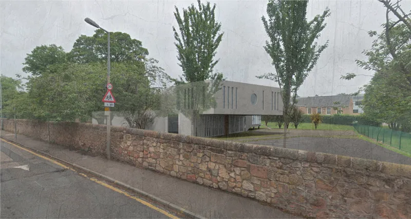 Street view of the facade with vertical window openings behind a stone retaining wall and mature trees in rain