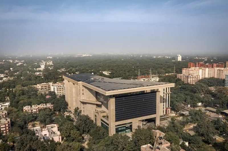 Aerial view of the building with its angled rooftop solar panels surrounded by residential neighborhoods and treetops