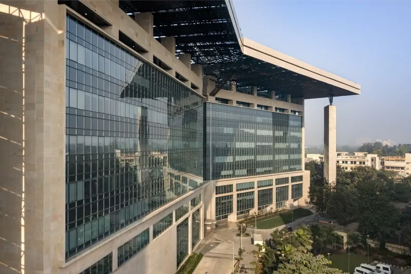 Glass curtain wall facade with exposed concrete columns and the cantilevered roof above a landscaped courtyard