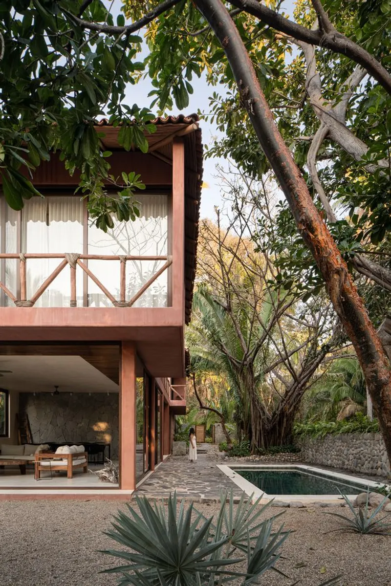 Two-story volume with timber balustrade and terracotta roof framed by overhanging tree branches