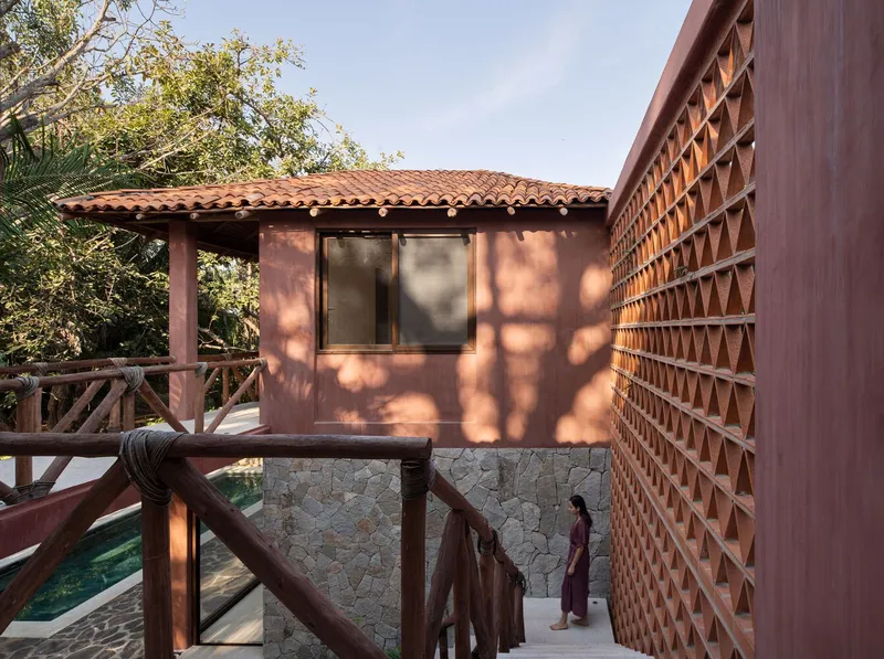 Terracotta-tiled roof pavilion and perforated brick screen wall with dappled shadows from surrounding trees