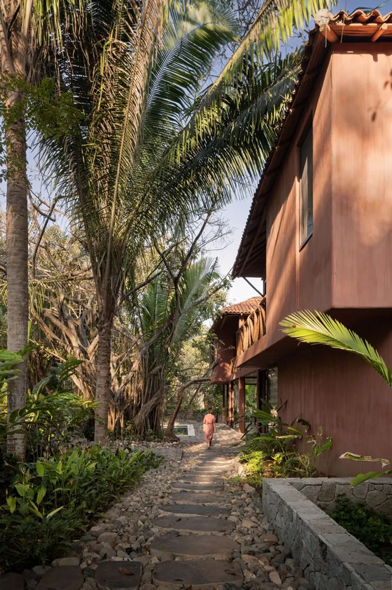 Stone paver pathway through planted beds leading between timber-clad volumes and palm trees