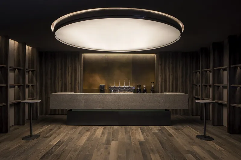 Tasting room with massive circular ceiling light over a floating concrete counter and timber shelving
