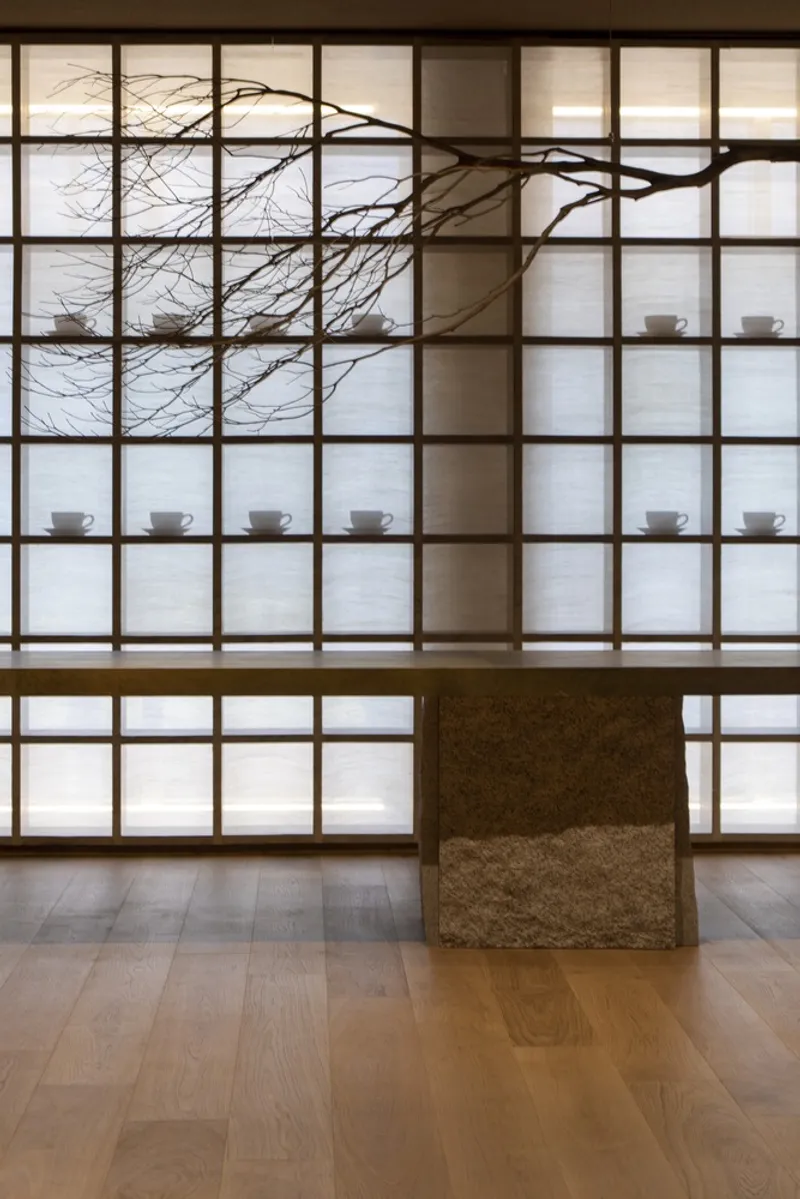 Gridded translucent wall with timber frame displaying ceramic cups and bare tree branches