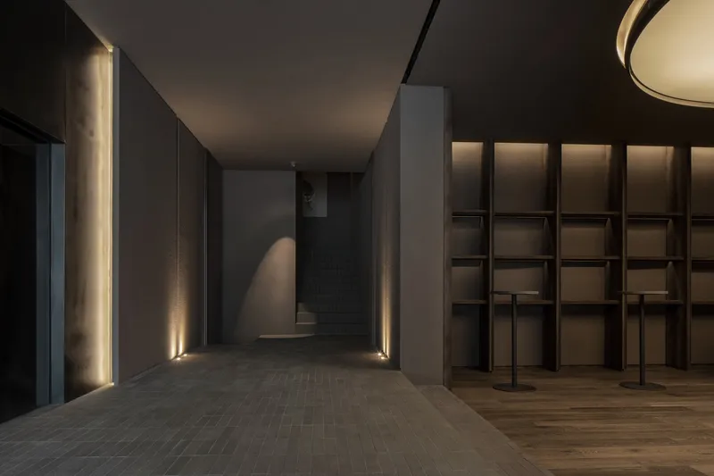 Corridor with vertical slot lighting flanking dark tile floor and recessed display shelving