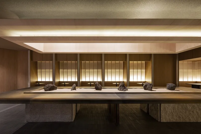 Long timber display table with natural stone objects set against backlit vertical wood paneling