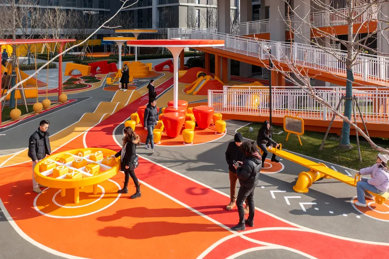Ground-level view of the play area with curved orange surfaces and families gathered under bare trees
