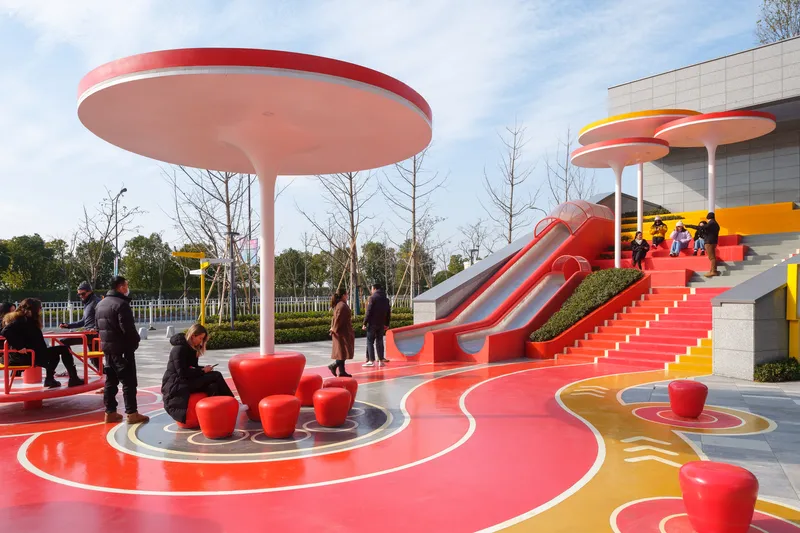 Pink circular canopy sheltering red molded seating elements on the patterned play surface