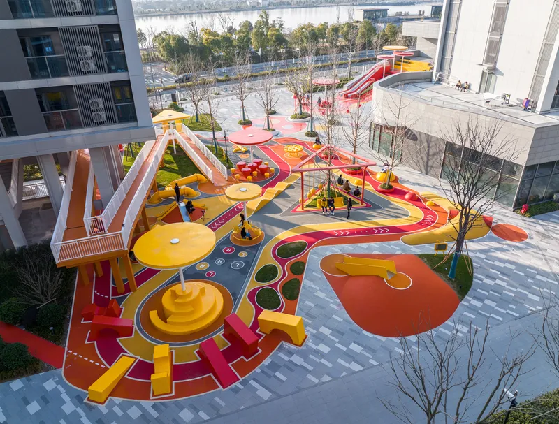 Aerial view of the outdoor playground with red and yellow play surfaces between residential buildings