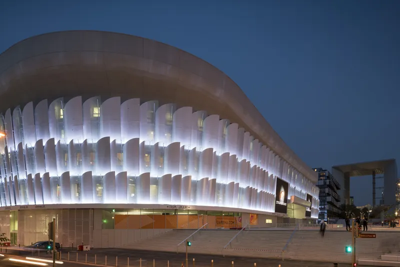 Illuminated facade with vertical louvered panels above a broad staircase at dusk