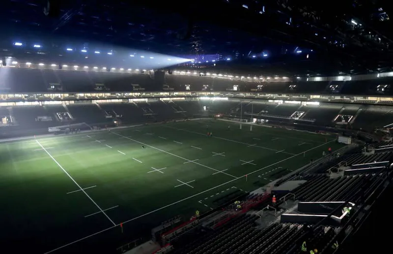 View across the seating tiers toward the playing field under exposed roof structure at night