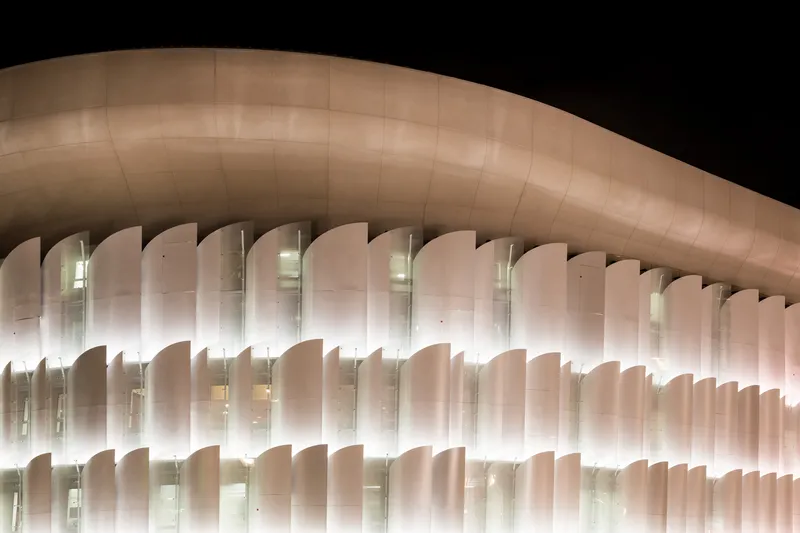 Close-up of the illuminated vertical fin facade beneath the curved roof at night