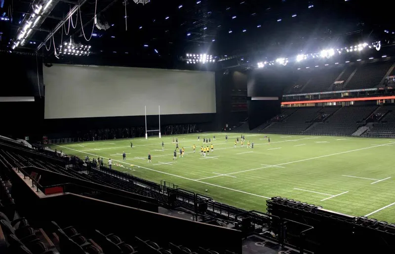Corner view showing the field, scoreboard and tiered seating with players on the pitch